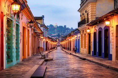 Illuminated colonial street at dusk with colorful buildings and lanterns
