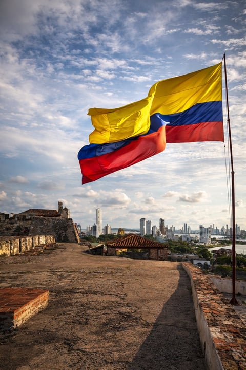 Colombian flag waving over historic fortress ruins with modern city skyline in background