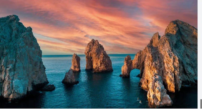 Dramatic rocky rock formations rising from turquoise ocean waters at sunset with golden and pink sky