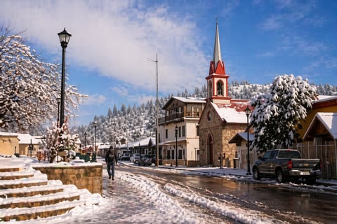 Snow-covered mountain village street with church steeple, historic buildings, and person walking past street lamp