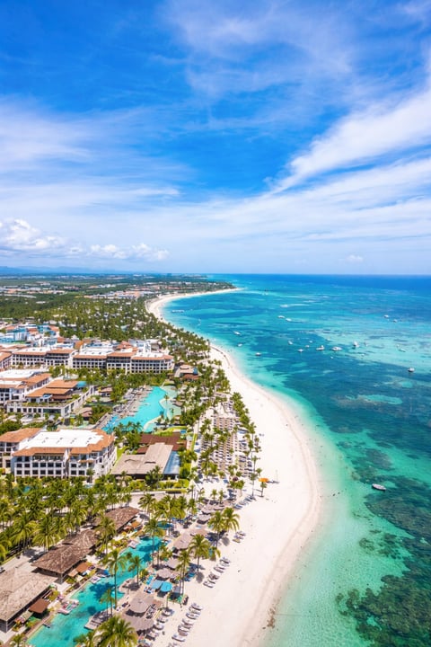 Aerial view of a tropical resort with white sand beach, turquoise ocean, pool, palm trees and hotels along the coastline
