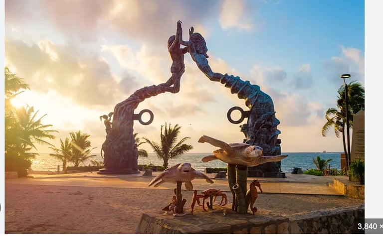 Two large bronze sculptures of intertwined figures on a beach at sunset, with palm trees and ocean in the background
